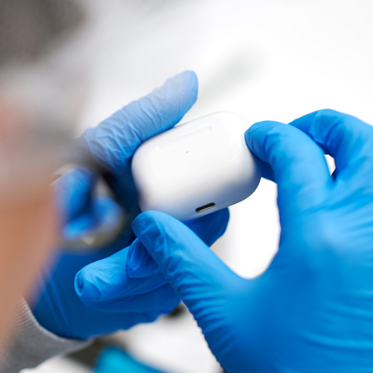 Two hands wearing latex gloves hold up an AirPods case